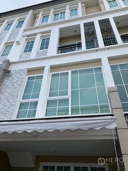 ทาวน์เฮาส์ ให้เช่าในBang Na, Bangkok - ด้านหน้าทาวน์เฮ้าส์หลายชั้น พร้อมหน้าต่างบานใหญ่และระเบียงเล็ก