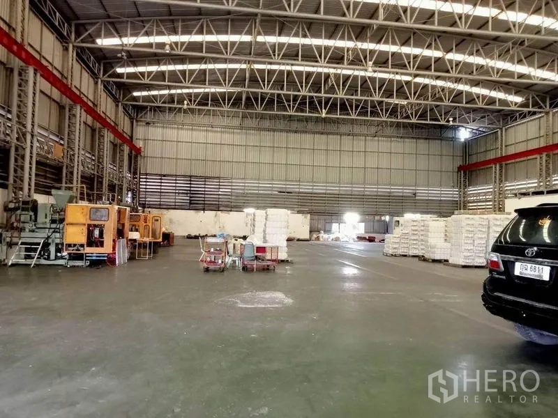Factory for rent in Bang Phli, Samut Prakan - Spacious warehouse hall with high steel-truss roof, concrete floor, machinery and stacked pallets.