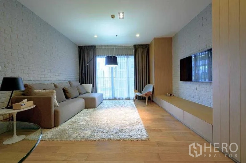 Condominium for rent in Watthana, Bangkok - Bright living room with brick feature walls, large sofa, TV wall and floor-to-ceiling window.