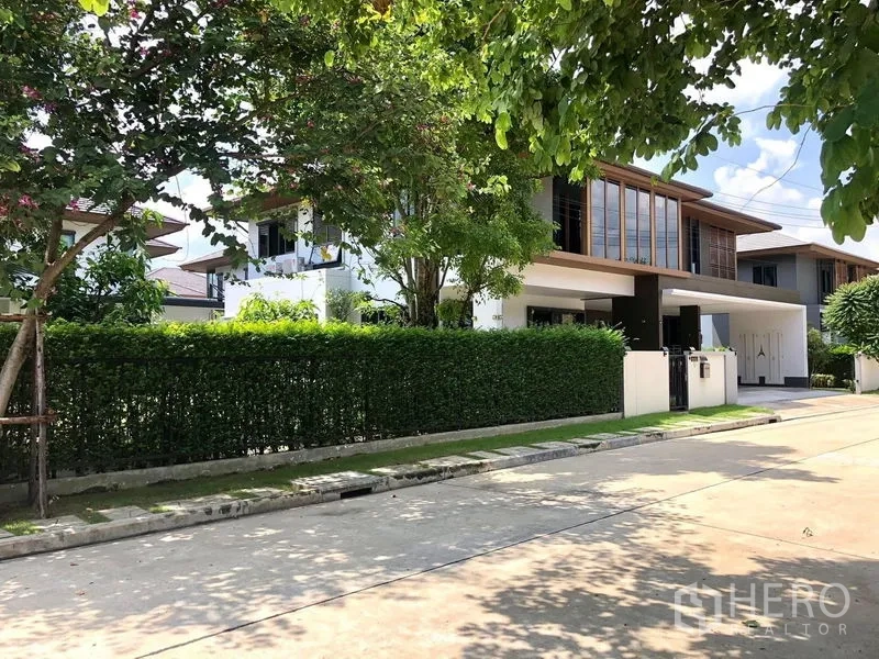 Detached House for rent or sale in Prawet, Bangkok - Tree-lined residential street view of the detached house with privacy hedge and sidewalk.
