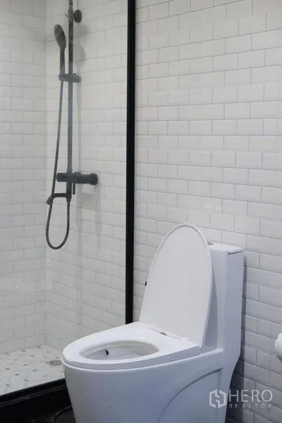 公寓 出租在Bang Rak, Bangkok - 现代浴室，白色地铁砖、玻璃淋浴间与坐便器。