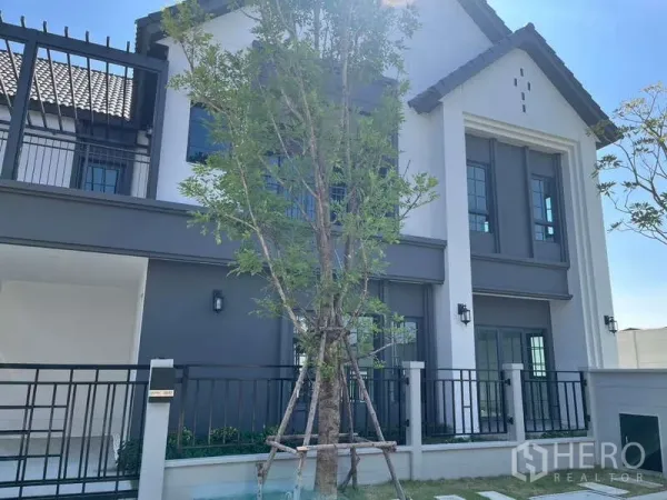 Detached House for rent in Bang Phli, Samut Prakan - Modern gabled detached house exterior with fenced front yard and a newly planted tree.