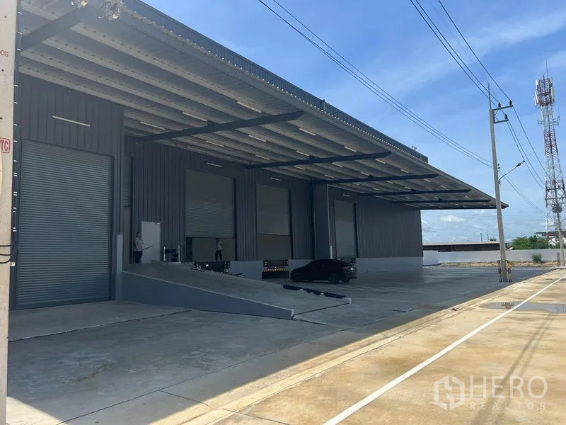 工厂 出租在Bang Pakong, Chachoengsao - 室外装卸区设长雨棚、卡车坡道、多扇卷帘门与宽阔车道。