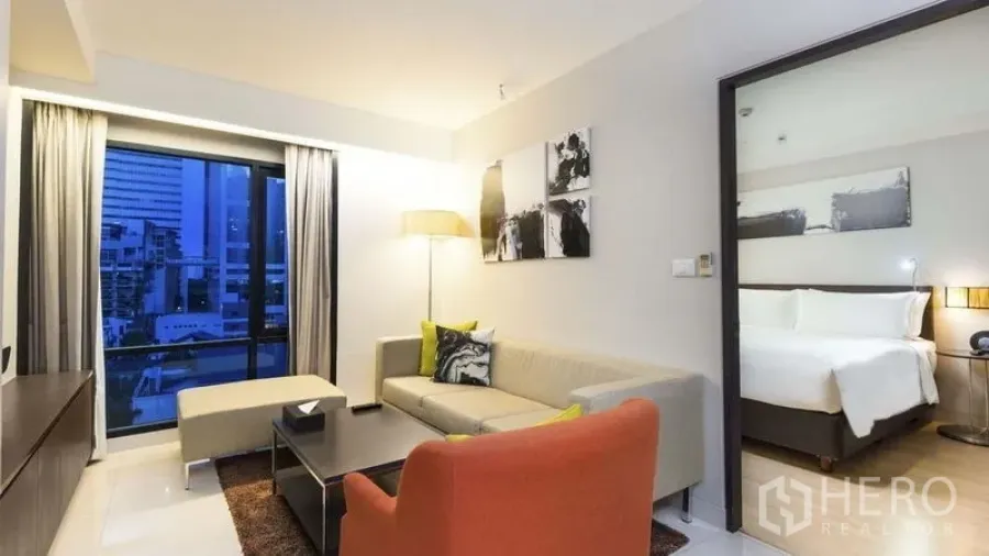 Apartment for rent in Watthana, Bangkok - Bright living room with city-view window, sofa and orange armchair next to the bedroom.