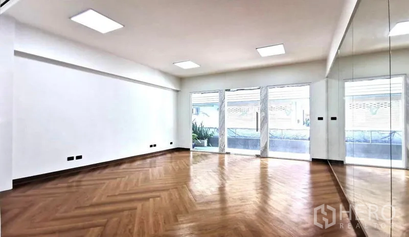 Home Office for rent in Watthana, Bangkok - Bright open-plan room with large sliding glass doors to a balcony, mirrors and wooden herringbone flooring.