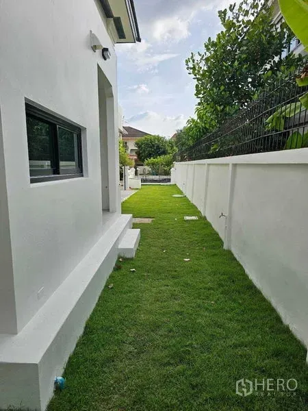 Detached House for sale in Thanyaburi, Pathum Thani - Green side yard with lawn stretching along the house and boundary wall.