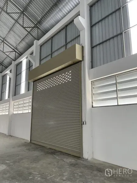 Factory for rent or sale in Bang Bo, Samut Prakan - Close-up of interior roller shutter door with ventilated window panels beside it.