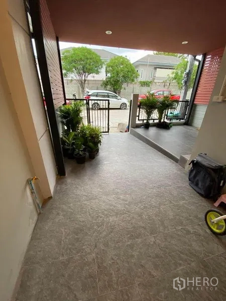 Townhouse for sale in Saphan Sung, Bangkok - Covered front porch and carport with potted plants and a gated entrance facing a quiet street.