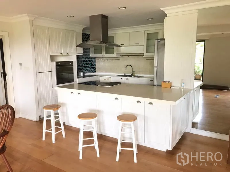Condominium for rent in Sathon, Bangkok - Spacious kitchen with large breakfast island and three stools, white cabinetry and stainless appliances.