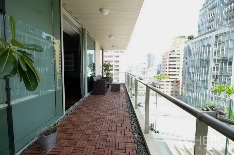 公寓 出租在Bang Rak, Bangkok - 长条玻璃栏杆阳台，户外座椅与盆栽，面向是隆高楼景观。