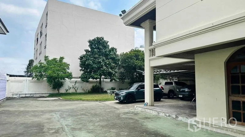 บ้าน ขายในHuai Khwang, Bangkok - ลานจอดรถคอนกรีตกว้าง พร้อมสนามหญ้าและต้นไม้ข้างบ้านเดี่ยวในห้วยขวาง กรุงเทพฯ มีที่จอดรถในร่ม