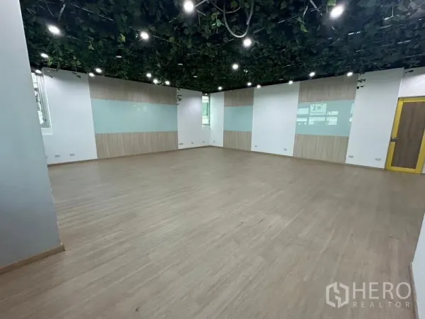 Office Space for rent in Ratchathewi, Bangkok - Large training room with wood-look floor and green ceiling vines and spotlights.