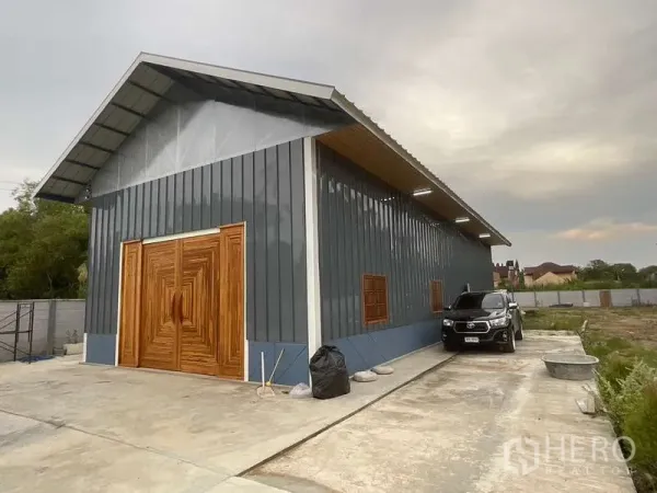 คลังสินค้า ให้เช่าหรือขายในNong Chok, Bangkok - ภาพมุมเอียงของโกดังยาว ผนังโลหะ พื้นที่จอดรถ และลานคอนกรีต