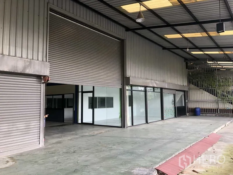 Warehouse for rent in Bang Phli, Samut Prakan - Covered loading bay with multiple roller shutters and a glass-fronted office entrance.