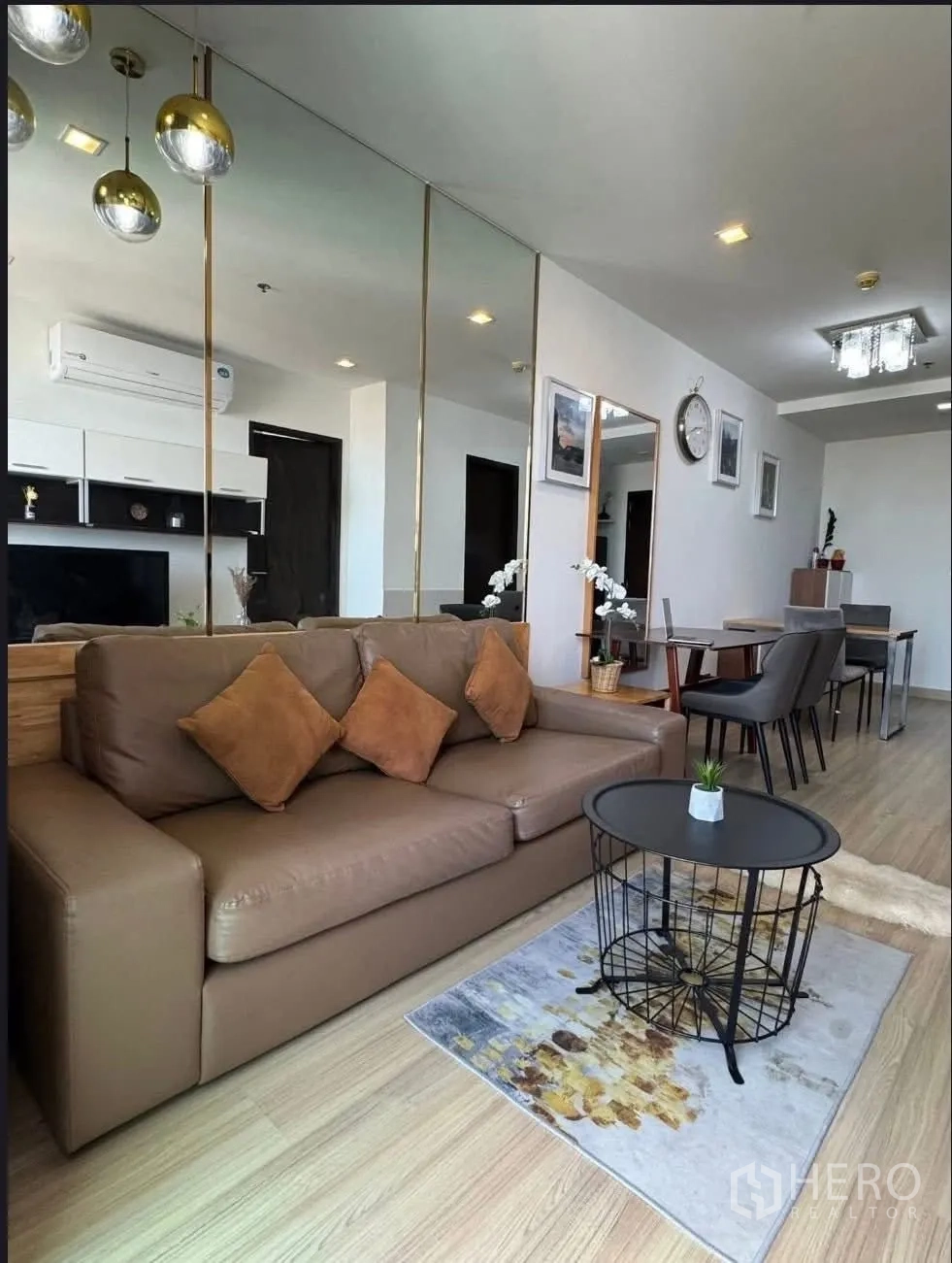 Condominium for rent in Watthana, Bangkok - Cozy lounge with brown leather sofa, mirrored feature wall, and pendant lights beside the dining table.