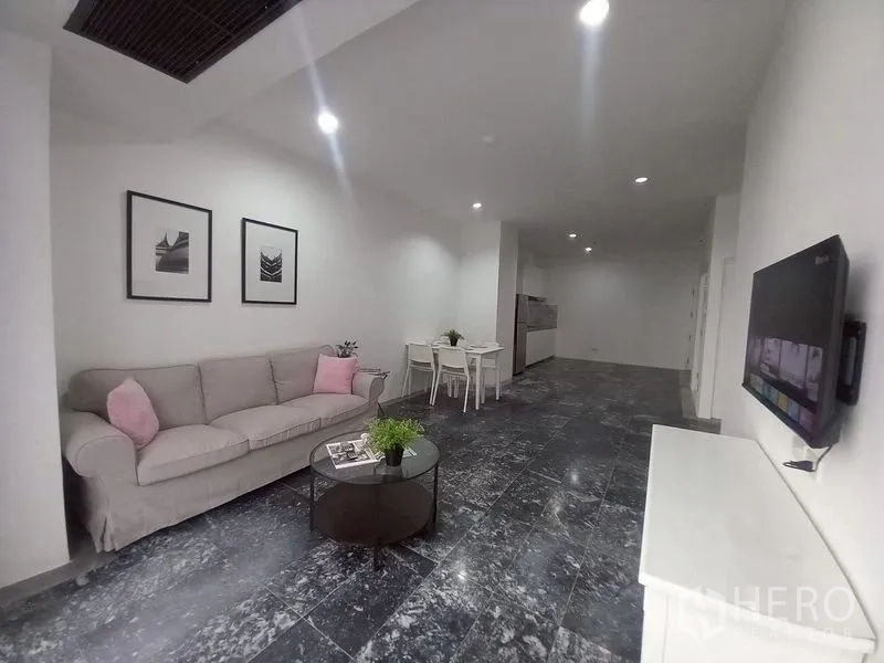 Condominium for rent in Watthana, Bangkok - Open-plan living room with sofa, dining set, wall-mounted TV and dark stone flooring.