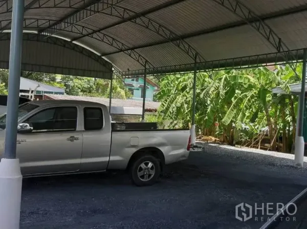 Land for sale in Mueang Samut Prakan, Samut Prakan - Large metal-roof carport on the land with a parked pickup truck and banana trees at the boundary.