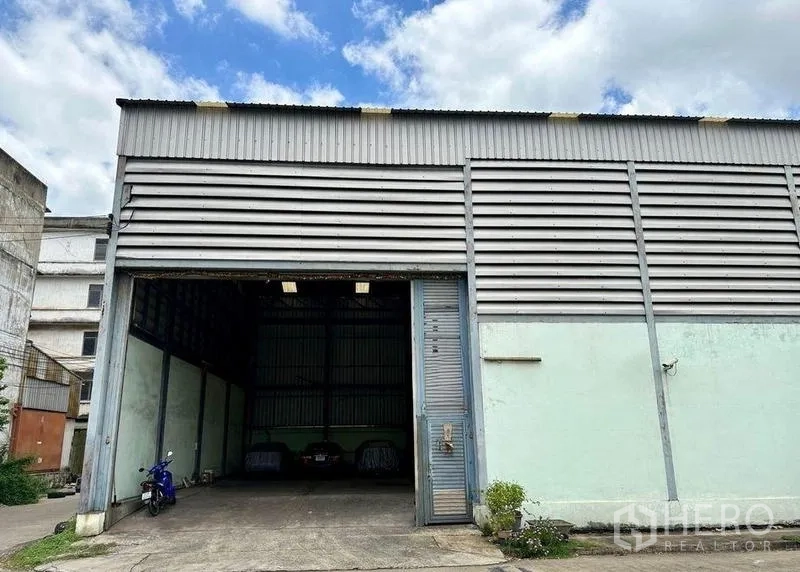 คลังสินค้า ขายในBang Bon, Bangkok - ด้านหน้าโกดังพร้อมประตูม้วนและลานคอนกรีตสำหรับจอดรถ
