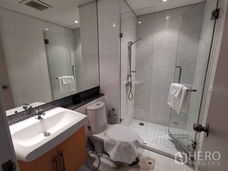 Condominium for rent in Watthana, Bangkok - Sleek bathroom with glass-enclosed shower, white tiles, and modern sanitary ware.