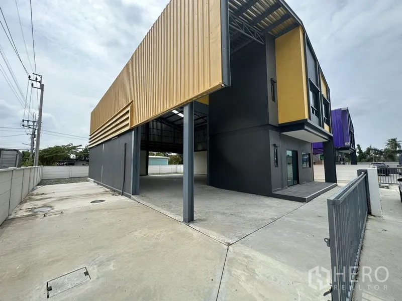 工厂 出租或出售在Bang Yai, Nonthaburi - 侧视图，带雨棚的装卸区、围栏大门与宽阔混凝土场地。