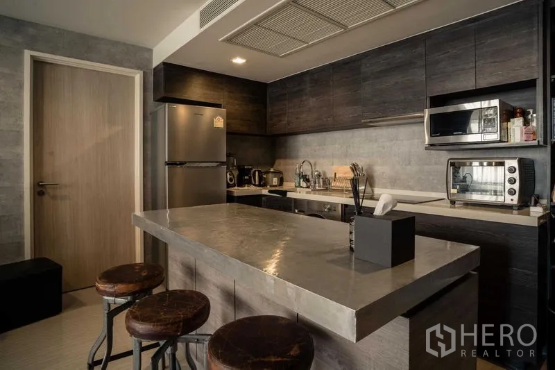 Condominium for sale in Watthana, Bangkok - Contemporary kitchen with stone island, dark cabinetry and stainless appliances.