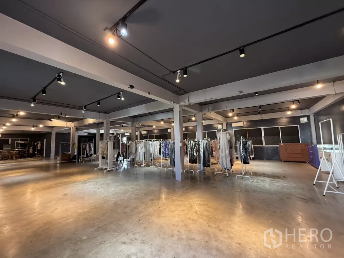 Office Space for rent in Wang Thonglang, Bangkok - Large studio-style office area with 4.9 m high ceiling, clothing racks and concrete flooring under spotlights.