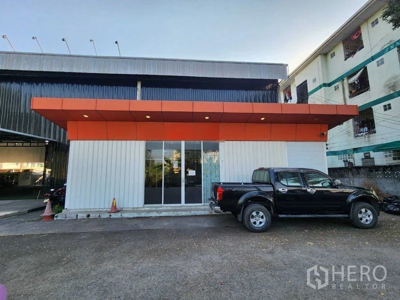 คลังสินค้า ให้เช่าในLat Phrao, Bangkok - มุมหน้าตึกออฟฟิศกั้นกระจก หลังคาสีส้ม มีรถกระบะจอดด้านหน้า