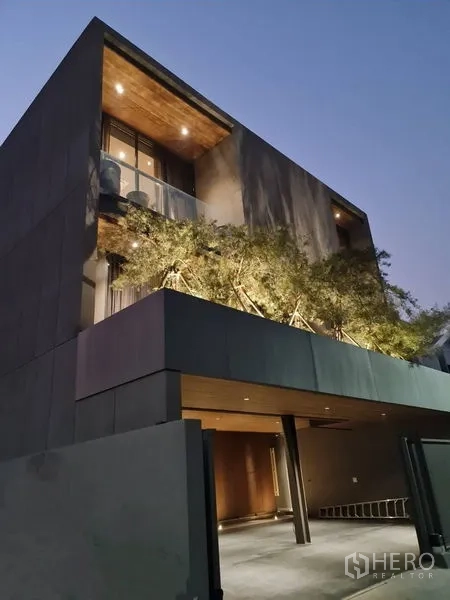 独立式住宅 出售在Lat Phrao, Bangkok - 低角度仰视入口，阳台绿植与暖色外墙灯光。