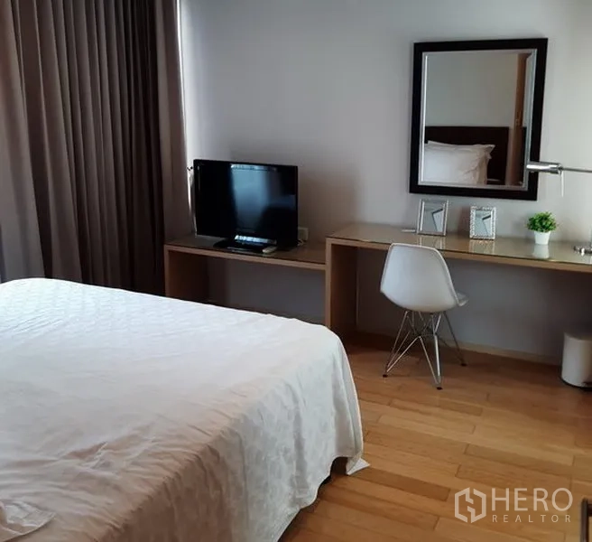 Condominium for rent in Khlong Toei, Bangkok - Master bedroom with TV, long built‑in desk, mirror and wood floors.