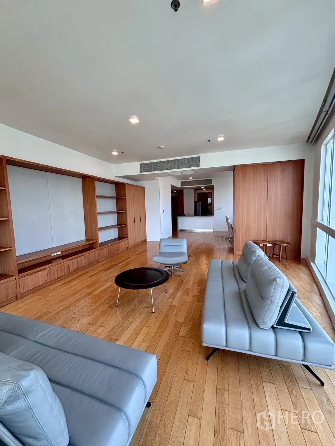 Condominium for rent in Khlong Toei, Bangkok - Spacious living room with grey leather sofas, round coffee table, and built-in media shelving.