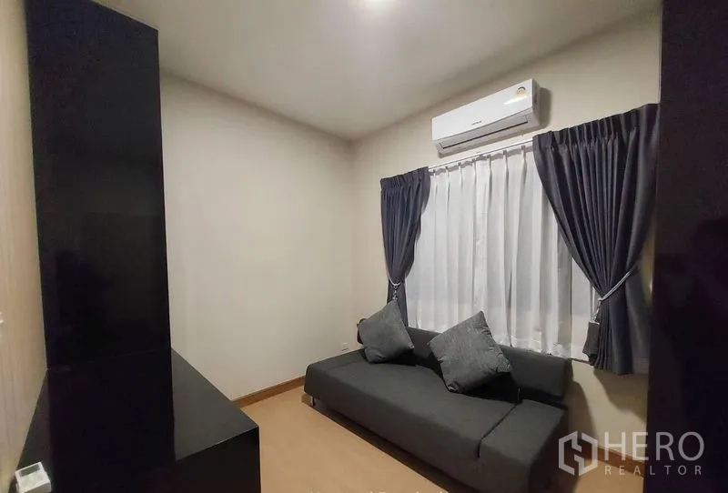 联排别墅 出租在Thanyaburi, Pathum Thani - 紧凑的客房，灰色沙发床、窗帘与壁挂空调