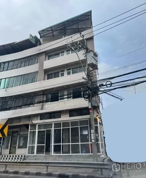 店屋 出租在Suan Luang, Bangkok - 转角联排商铺外观，落地窗与多层结构，行人道旁有架空线缆。