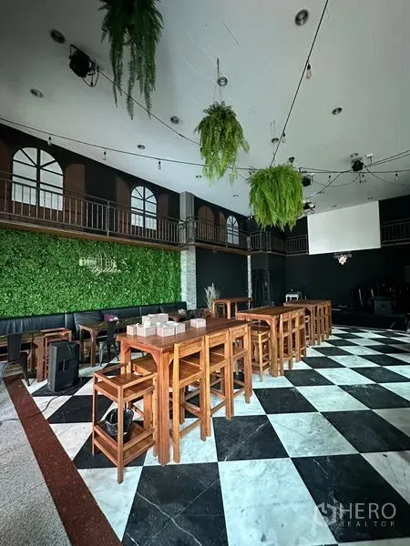 Retail Space for rent in Suan Luang, Bangkok - Spacious indoor hall with black-and-white checkerboard floor, long wooden tables, hanging plants and stage with screen.