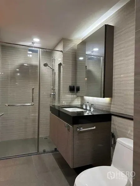 Condominium for sale in Pathum Wan, Bangkok - Contemporary bathroom featuring a glass-enclosed shower, illuminated vanity and wall mirror.