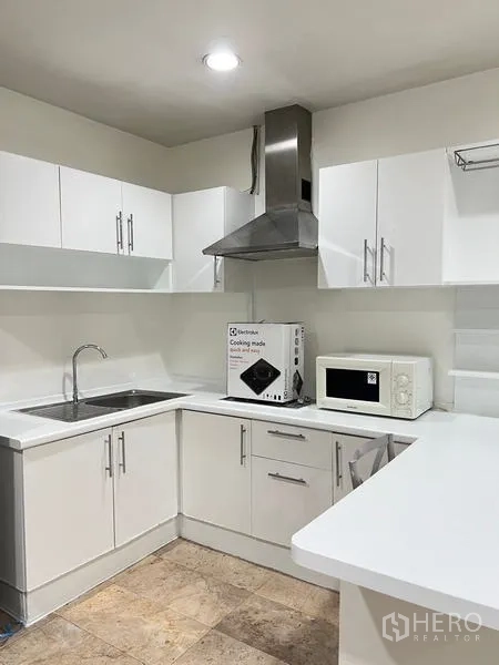 Condominium for rent in Ratchathewi, Bangkok - Bright L-shaped white kitchen with hood, sink and microwave.