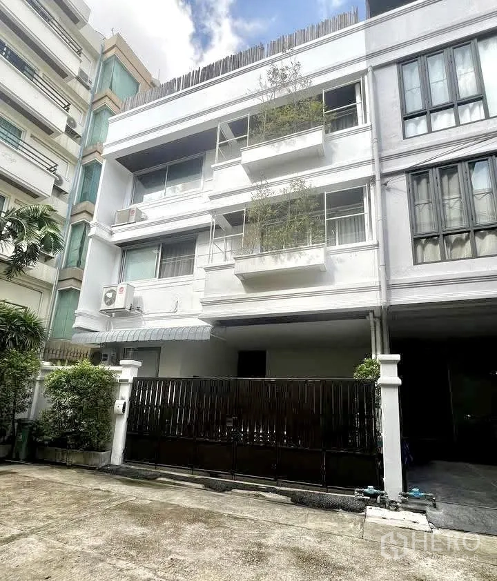 ทาวน์เฮาส์ for rent or sale in Watthana, Bangkok - อาคารทาวน์เฮ้าส์สีขาวสี่ชั้นพร้อมระเบียงและประตูรั้วที่จอดรถ