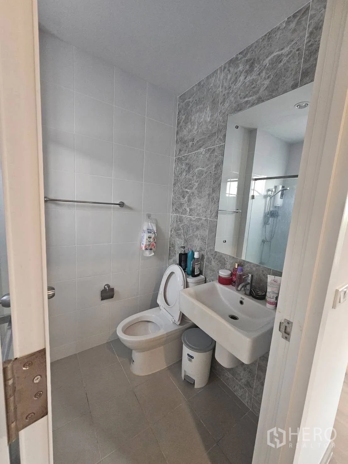 Detached House for rent in Khlong Sam Wa, Bangkok - Second bathroom with gray accent tiles, basin, toilet and glass shower.