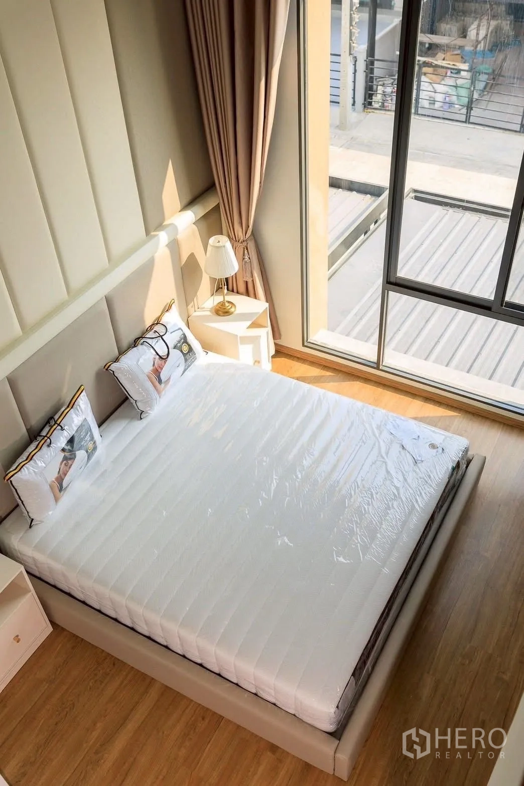 Townhouse for rent or sale in Bang Phli, Samut Prakan - Sunlit bed beside a full-height window with beige curtains and warm wood flooring.
