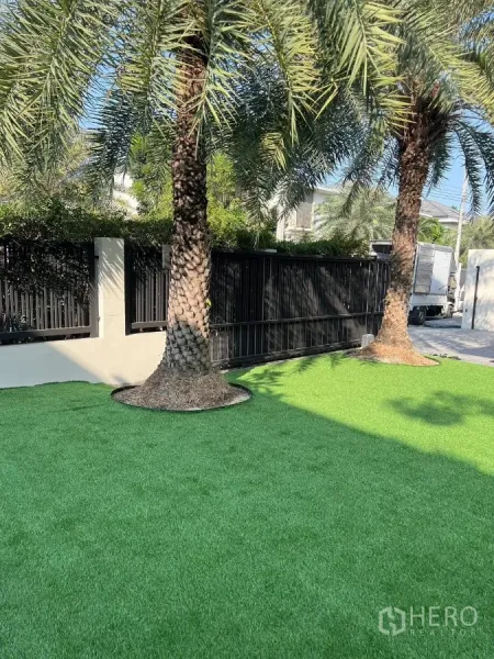 独立式住宅 出租在Bang Phli, Samut Prakan - 前庭棕榈树与人造草坪，旁有黑色大门