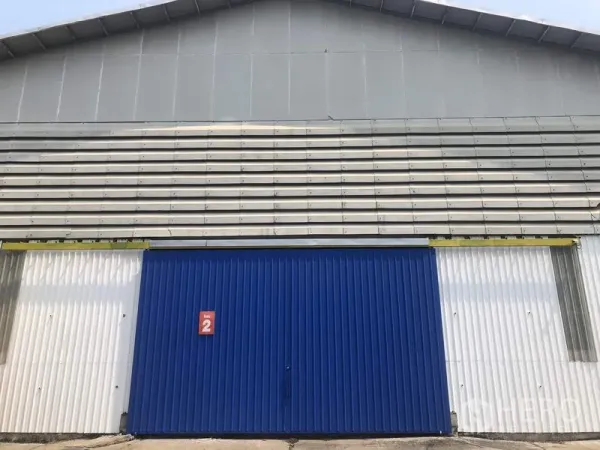 Warehouse for rent in Pak Kret, Nonthaburi - Front view of the warehouse facade with a wide blue sliding door and corrugated metal panels