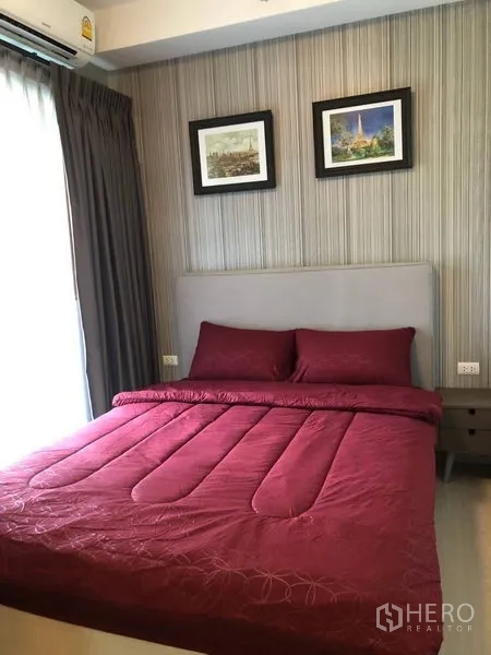 Condominium for rent or sale in Huai Khwang, Bangkok - Bright bedroom with a double bed in red bedding, padded headboard, curtains, wall art, and air conditioner.