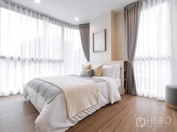 Condominium for rent in Watthana, Bangkok - Bright corner bedroom with floor-to-ceiling windows, sheer curtains and wood flooring.