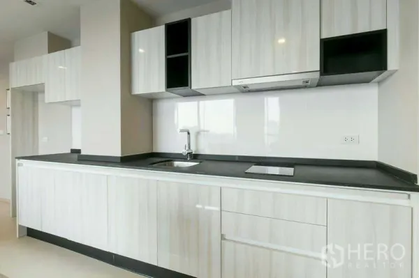 Condominium for rent or sale in Watthana, Bangkok - Modern linear kitchen with light wood cabinetry, black countertop, sink and electric cooktop.