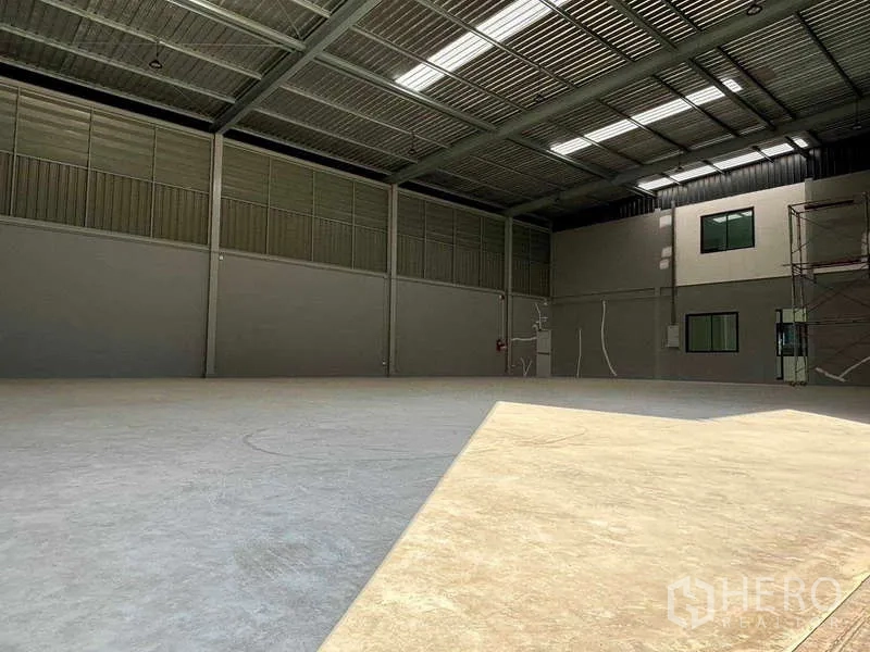Factory for rent in Bang Bo, Samut Prakan - High‑clear warehouse interior with steel roof structure and two‑storey office block at the back.