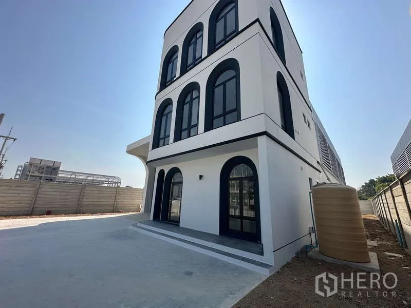 โรงงาน ขายในLam Luk Ka, Pathum Thani - มุมข้างอาคารออฟฟิศ หน้าต่างโค้ง ลานคอนกรีต และถังเก็บน้ำข้างกำแพง