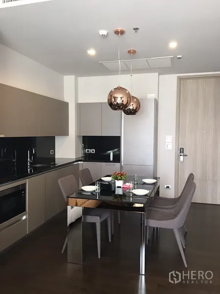 Condominium for rent in Watthana, Bangkok - Open-plan kitchen and dining area with black glass-top table set for four and copper pendant lights.