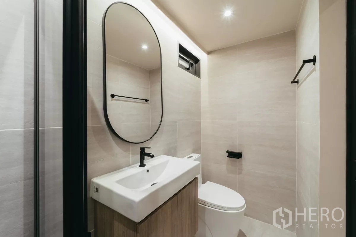 联排别墅 出租在Watthana, Bangkok - 小型盥洗室，椭圆镜、黑色五金与简洁浴柜。