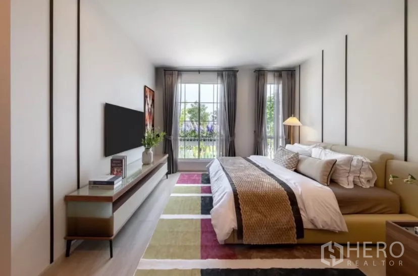 Townhouse for rent in Bang Phli, Samut Prakan - Master bedroom with king bed, full‑height windows, balcony and TV console.
