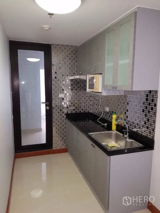 คอนโด ให้เช่าในWatthana, Bangkok - ครัวปิดแบบทางเดิน ผนังกระเบื้องโมเสก เคาน์เตอร์สีดำ ตู้บานกระจก อ่างล้างจาน และประตูสู่โซนบริการ