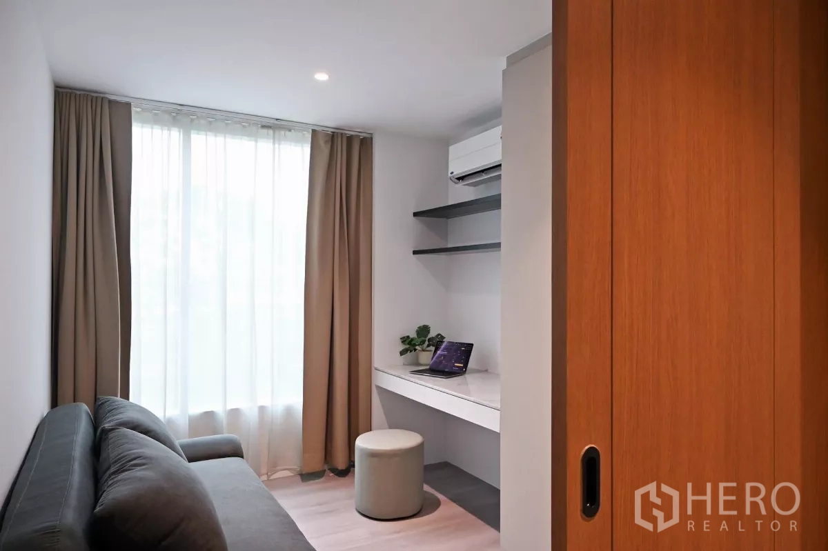 Condominium for rent in Watthana, Bangkok - Multi-purpose room or home office with desk, shelves, sofa and floor-to-ceiling window with curtains.